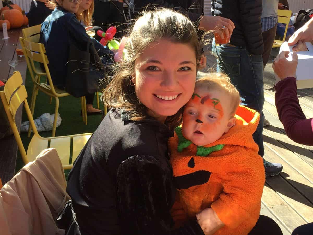 Toddler in a pumpkin costume with pumpkin face paint