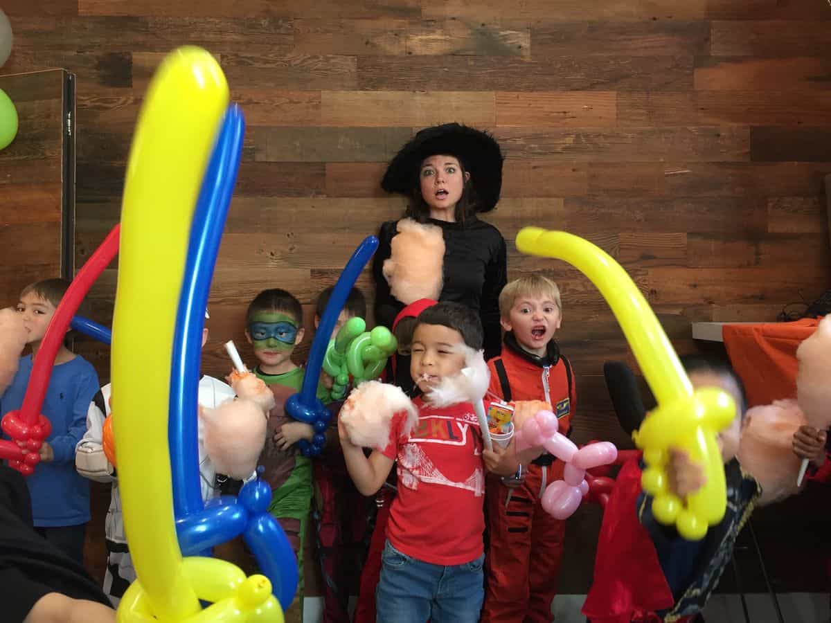 Children holding colorful balloon animals at a party with a clown performer.